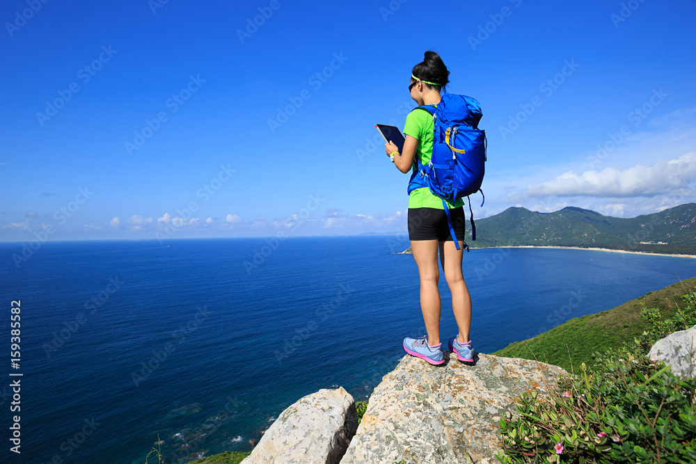 successful woman backpacker use digital tablet on seaside mountain rock