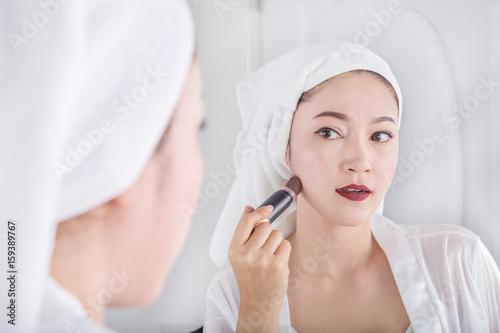 woman looking in the mirror and applying cosmetic with brush