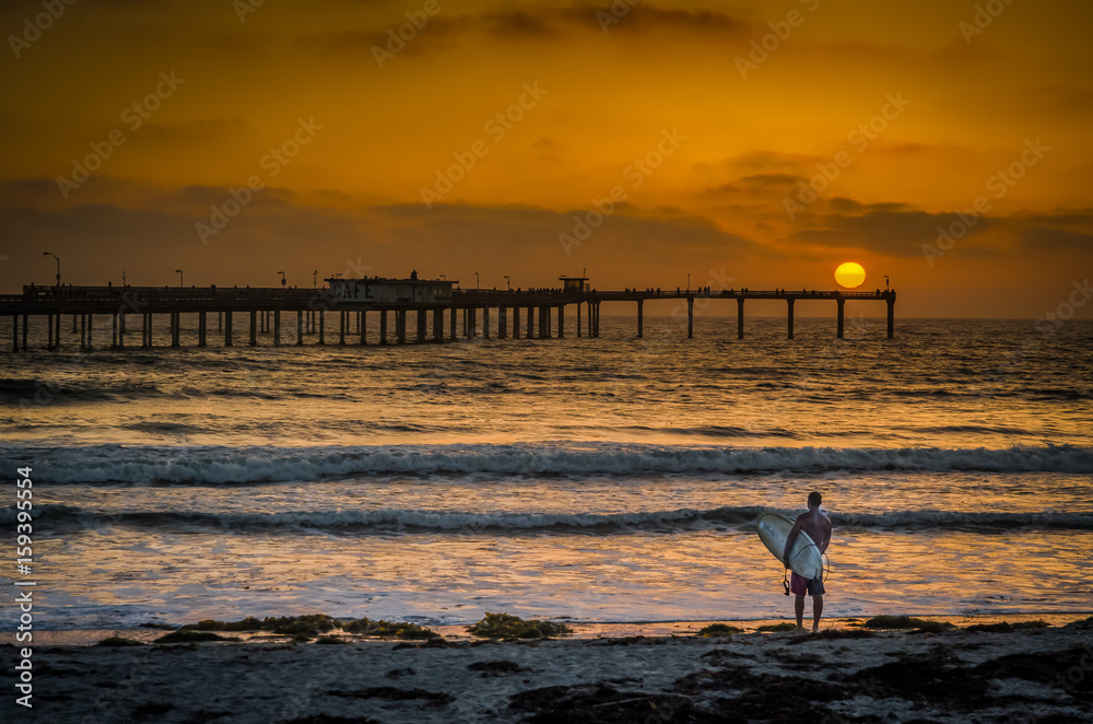 Surfer on California beach at sunset with pier