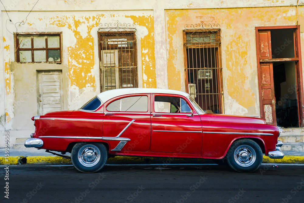 Vibrant red shiny car and ruined house in Cuba