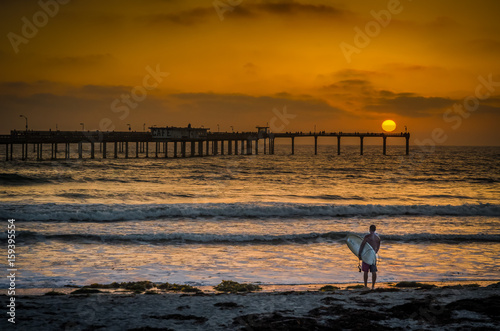 Surfer on California beach at sunset with pier