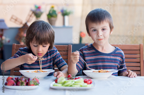 Cute children, preschool boys, eating spaghetti for lunch outdoors in garden