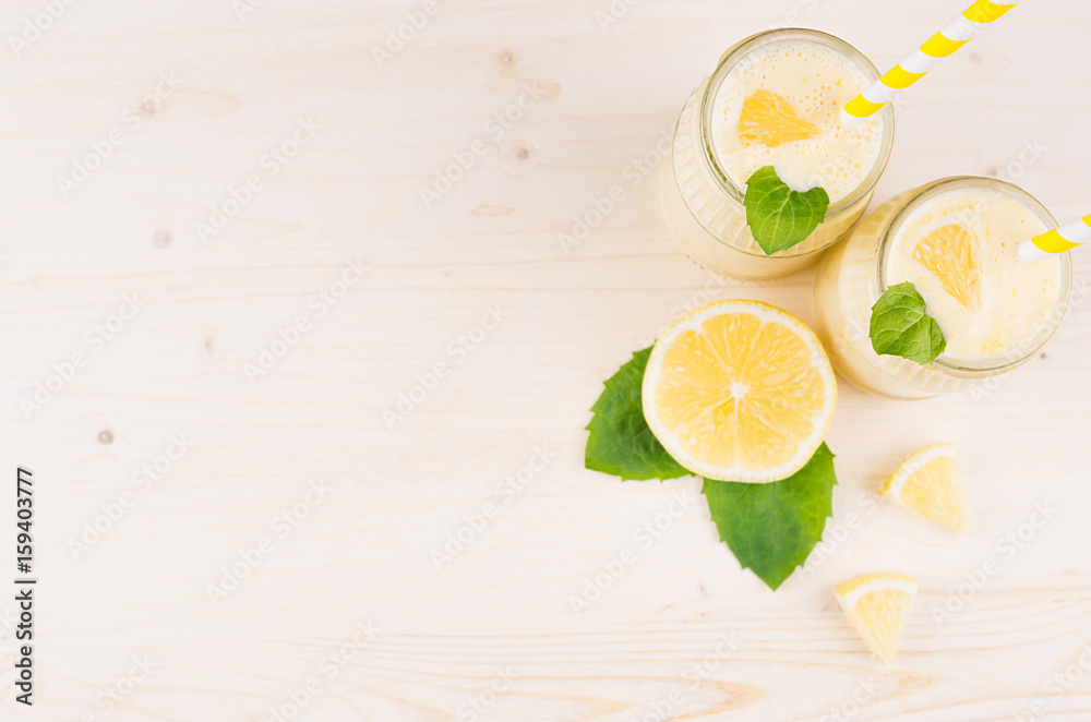 Decorative frame of yellow lemon smoothie in glass jars with straw, mint leaf, cut lemon, top view. White wooden board background, copy space. Decorative frame of yellow lemon smoothie in glass jars with straw, mint leaf, cut lemon, top view. White wooden board background, copy space.