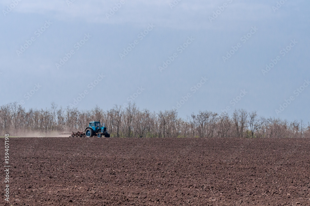An old tractor in the field plows the land. Spring landscape of a countryside, a farm. An old tractor in the field plows the land. Spring landscape of a countryside, a farm.