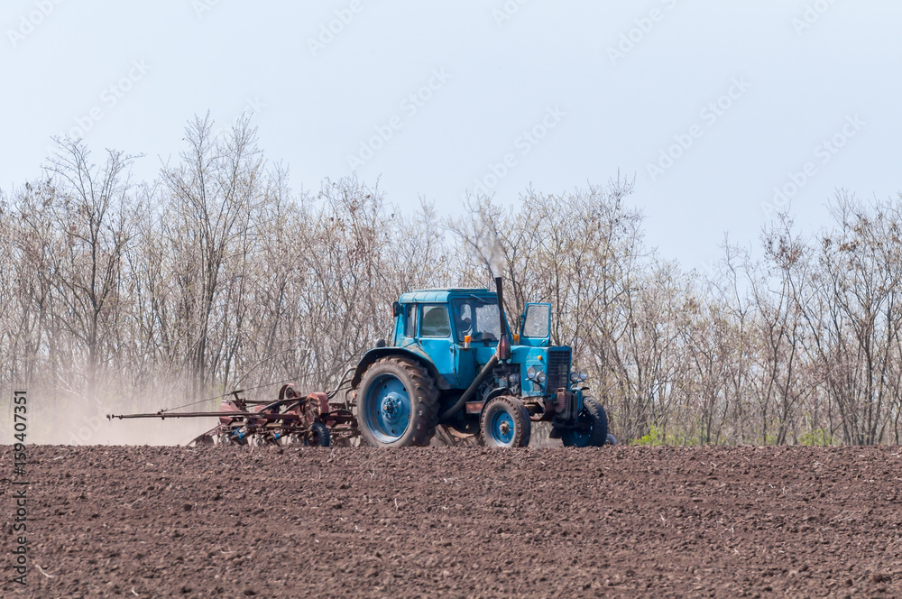 Obraz premium An old tractor in the field plows the land. Spring landscape of a countryside, a farm.