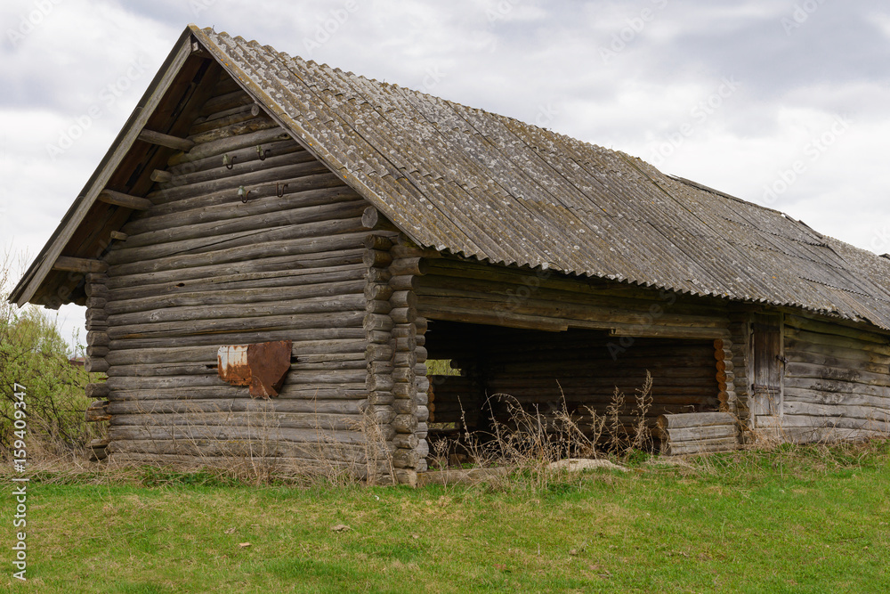 Old abandoned wooden house on a green lawn in cloudy weather