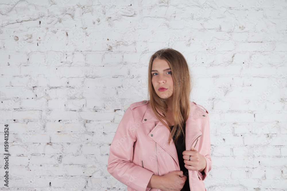 Beautiful young woman on leather jacket. Fashion model in pink leather jacket. Posing near white brick wall. Beautiful young woman on leather jacket. Fashion model in pink leather jacket. Posing near white brick wall.