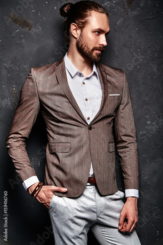 portrait of handsome fashion stylish hipster businessman model dressed in elegant brown suit posing near dark wall in studio