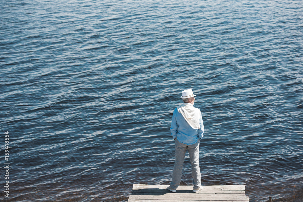 back view of casual man standing on quay in front of water surface at daytime