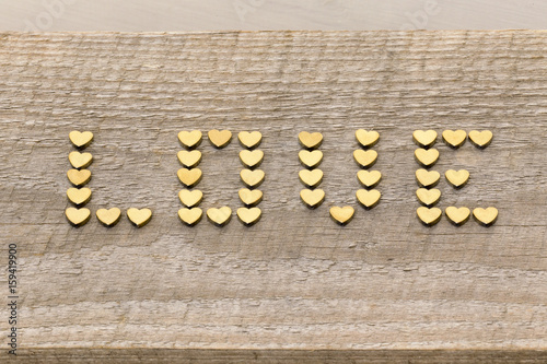 Word 'Love' made of golden hearts on old weathered wood background