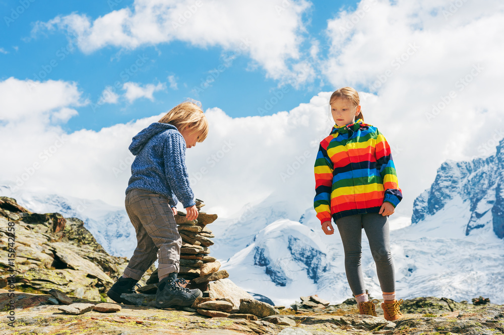 Cute little kids resting in Gornergrat glacier, Switzerland, Two young children playing together in mountains, small boy and his big sister hiking in swiss Alps, wearing colorful clothes