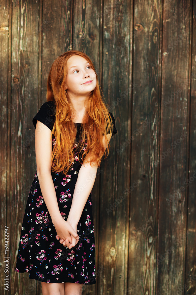 Fototapeta premium Outdoor fashion portrait of happy red-haired girl, posing against old wooden background