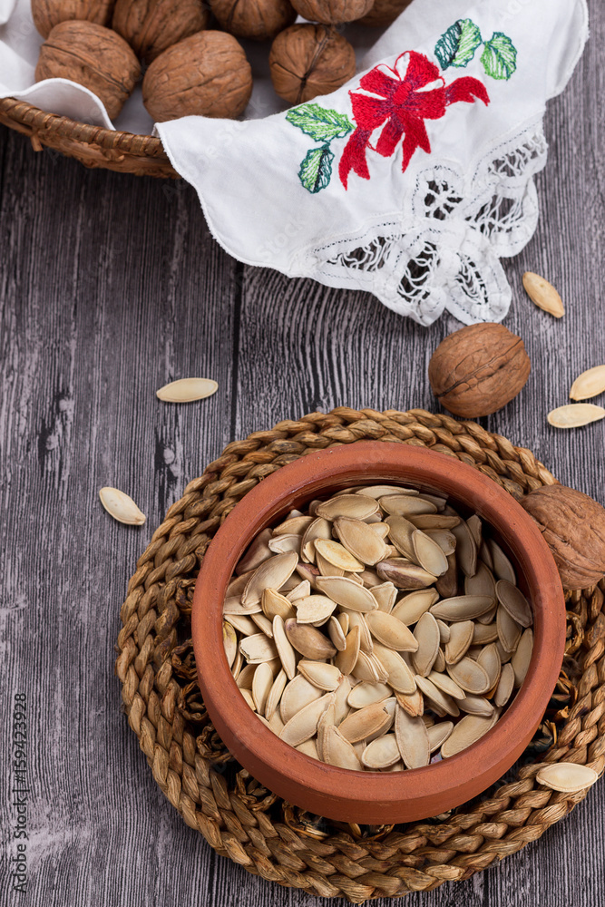 Vertical capture of pumpkin seeds in earthenware pot and walnuts in basket on wooden table Vertical capture of pumpkin seeds in earthenware pot and walnuts in basket on wooden table