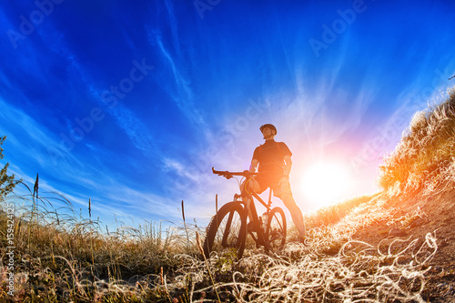 Low angle view of cyclist standing with mountain bike on trail at sunrise.