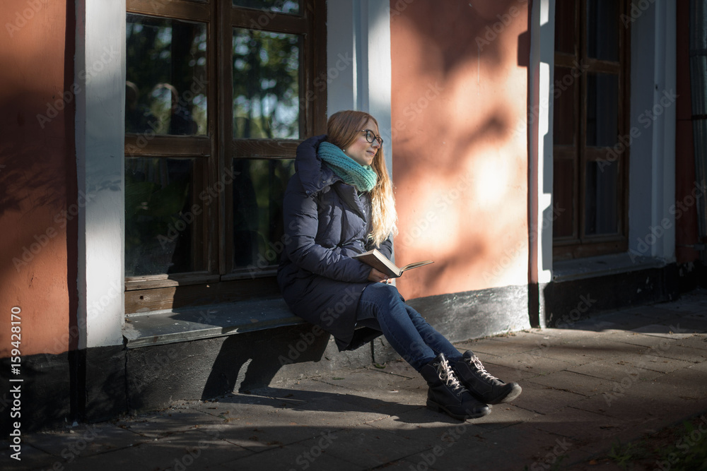 The girl is reading a book sitting by the window