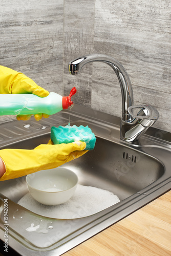 Hands in gloves washing tableware with sponge and detergent