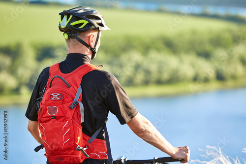 Rear view and close-up of the cyclist standing with mountain bike against river.