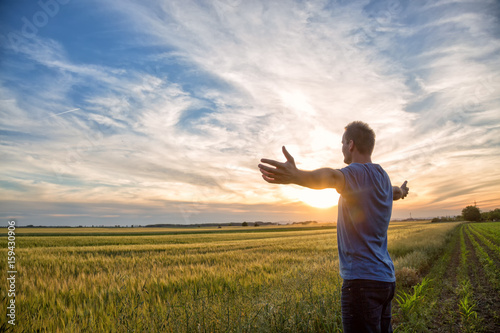 Man standing in an open field at sunset with open arms - embracing nature