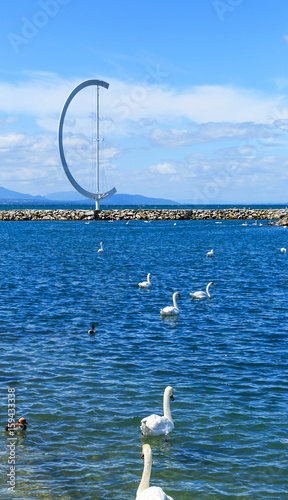 Entrance to the harbor Ouchi with the beautiful swans, stone mole, big symbol and blue spring sky on the background. Lausanne Switzerland photo