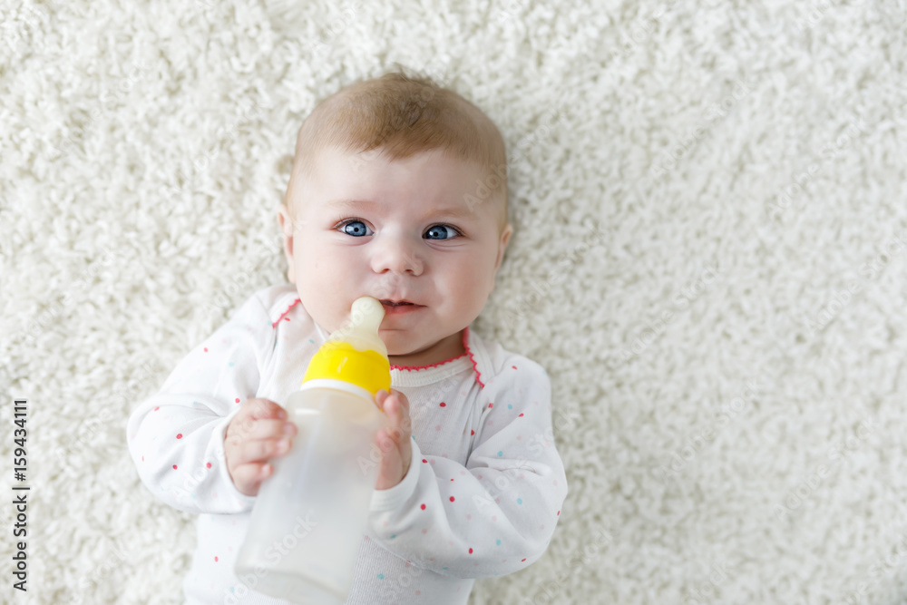 Cute adorable ewborn baby girl holding nursing bottle and drinking formula milk Cute adorable ewborn baby girl holding nursing bottle and drinking formula milk