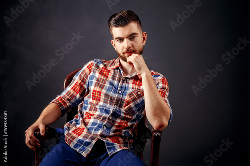 Portrait of bearded male with long hair sitting on chairand looking at camera over dark background in studio. photo