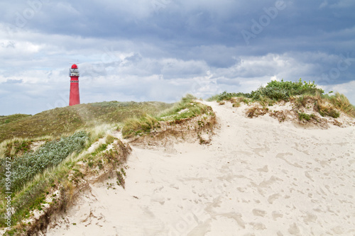 Red lighthouse in the dunes on a windy day, sand blowing in the air photo