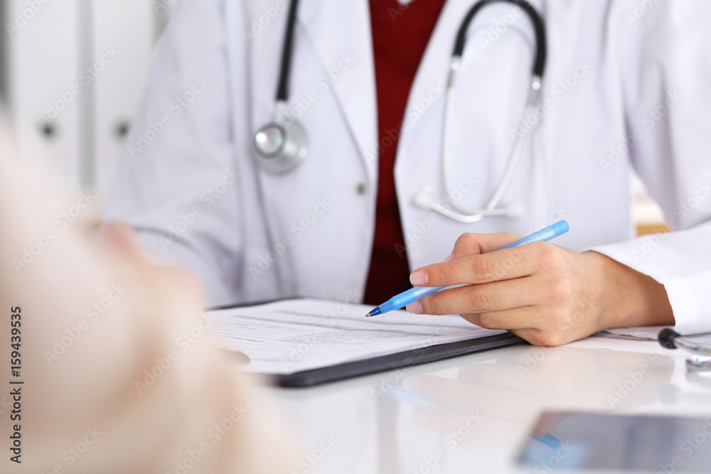 Close up of a female doctor filling up an application form while consulting patient Close up of a female doctor filling up an application form while consulting patient
