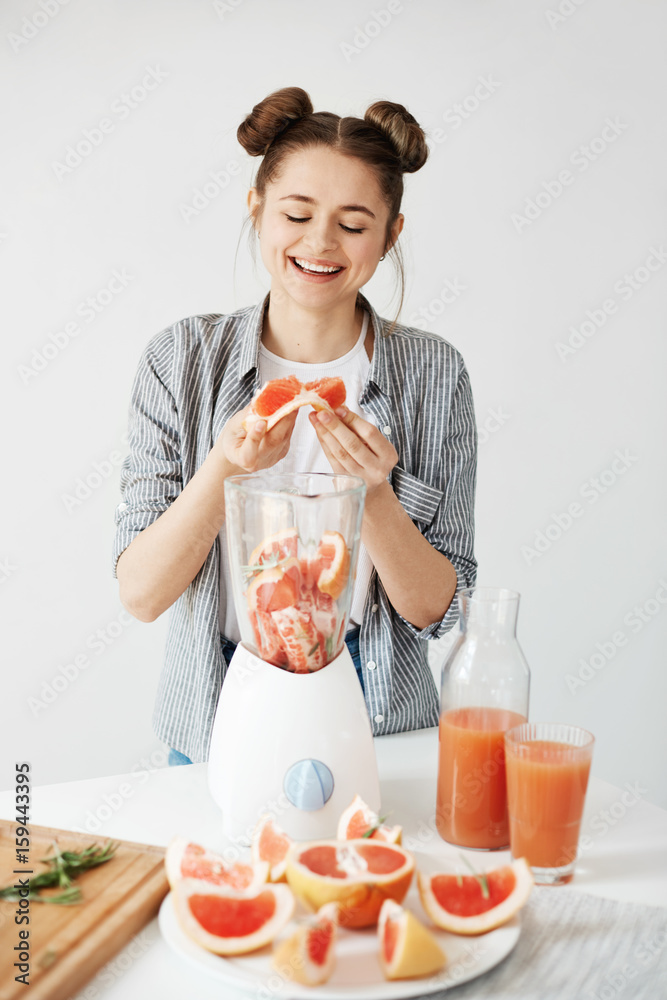 Pretty young girl smiling blending detox refreshing grapefruit smoothie over white wall. Healthy food concept. Pretty young girl smiling blending detox refreshing grapefruit smoothie over white wall. Healthy food concept.