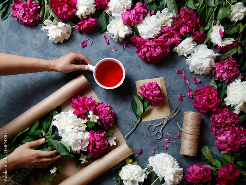 Tools and accessories florists need for making up a bouquet out of peonies: kraft paper, scissors, string, karkade tea, an envelopeon the table. Florist at work. View from above.