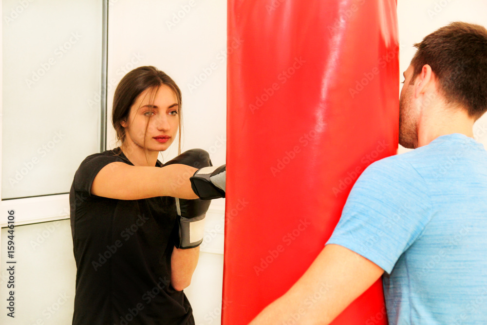 The female boxer training at gym. Young sporty woman punching her male partner with red boxing gloves at gym club. Attractive sports girl is practicing with a handsome trainer in the sport center.