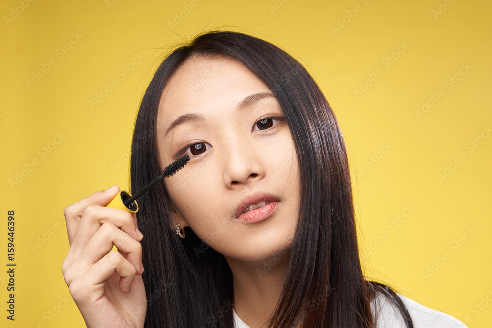 Woman paints her eyelashes with mascara on a yellow background Woman paints her eyelashes with mascara on a yellow background