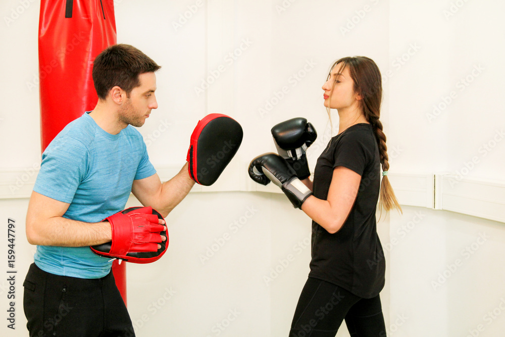 The female boxer training at gym. Young sporty woman punching her male partner with red boxing gloves at gym club. Attractive sports girl is practicing with a handsome trainer in the sport center. The female boxer training at gym. Young sporty woman punching her male partner with red boxing gloves at gym club. Attractive sports girl is practicing with a handsome trainer in the sport center.