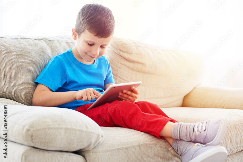 Small boy looking and touching a screen of a tablet Small boy looking and touching a screen of a tablet