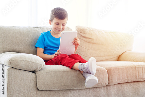 Smiling boy with tablet relaxing on the sofa