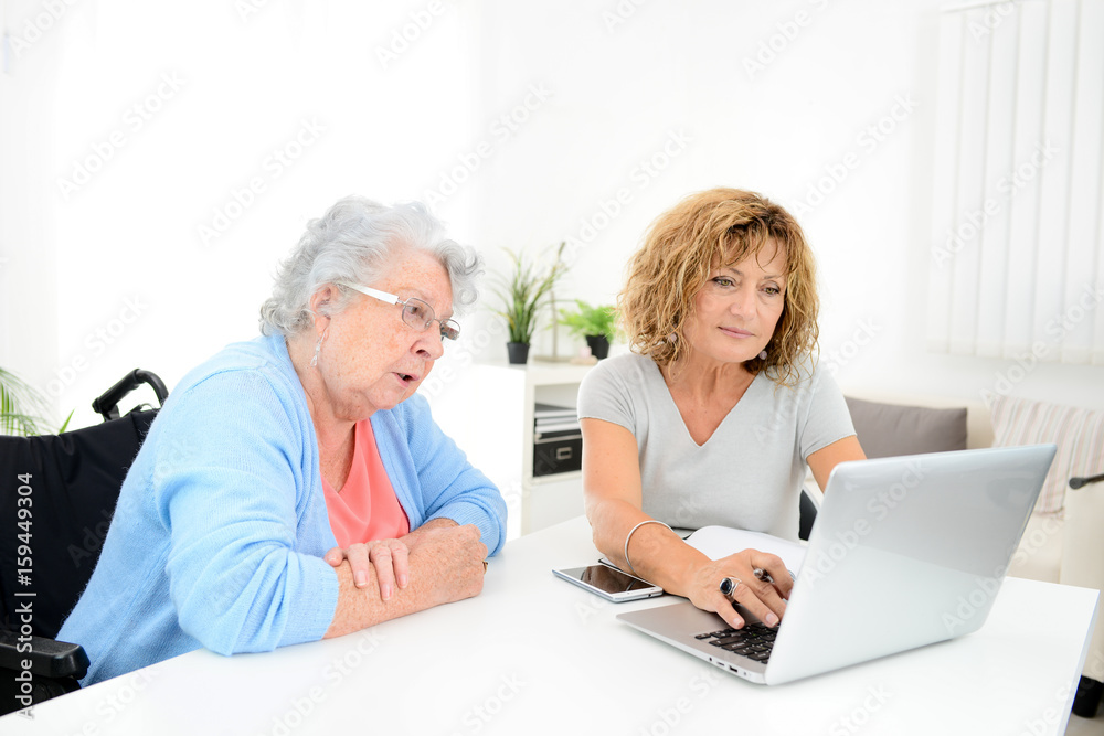 mature woman helping assisted elderly senior female with administrative procedures and paperwork on internet with a laptop computer at home mature woman helping assisted elderly senior female with administrative procedures and paperwork on internet with a laptop computer at home