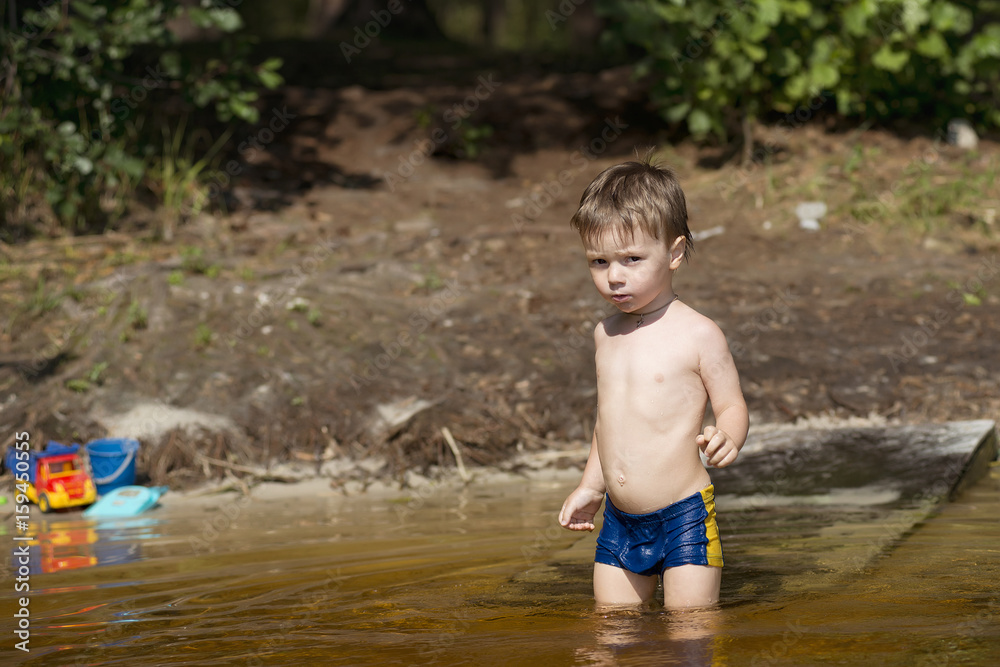 little boy in blue suit walks into the water of a lake on a summer day little boy in blue suit walks into the water of a lake on a summer day