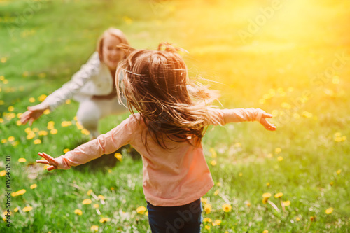 Child running into mother's hands to hug her. Family having fun in the park. Girl is happy to meet her mom. Background image.