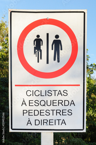Info board in Portuguese signaling that cyclists should ride on the left and pedestrians should walk on the right. In Portuguese: ciclistas a esquerda e pedestres a direita.