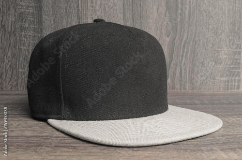 Leinwand Poster Black cap with light gray flap on a wooden background