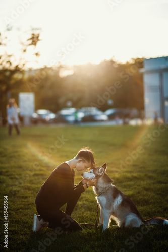 Fototapeta Naklejka Na Ścianę i Meble -  Beautiful young woman playing with funny husky dog outdoors in park at sunset  or sunrise 