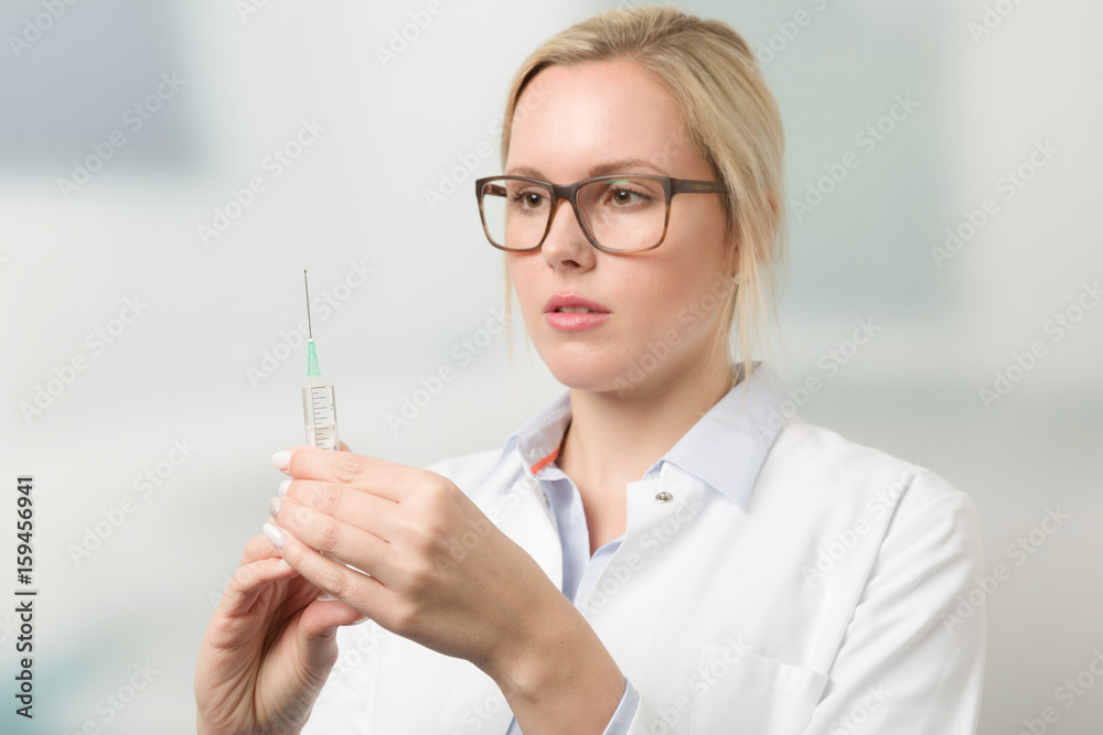 Junge hübsche Ärztin zieht Spritze aufmit Praxis im Hintergrund Junge hübsche Ärztin zieht Spritze aufmit Praxis im Hintergrund