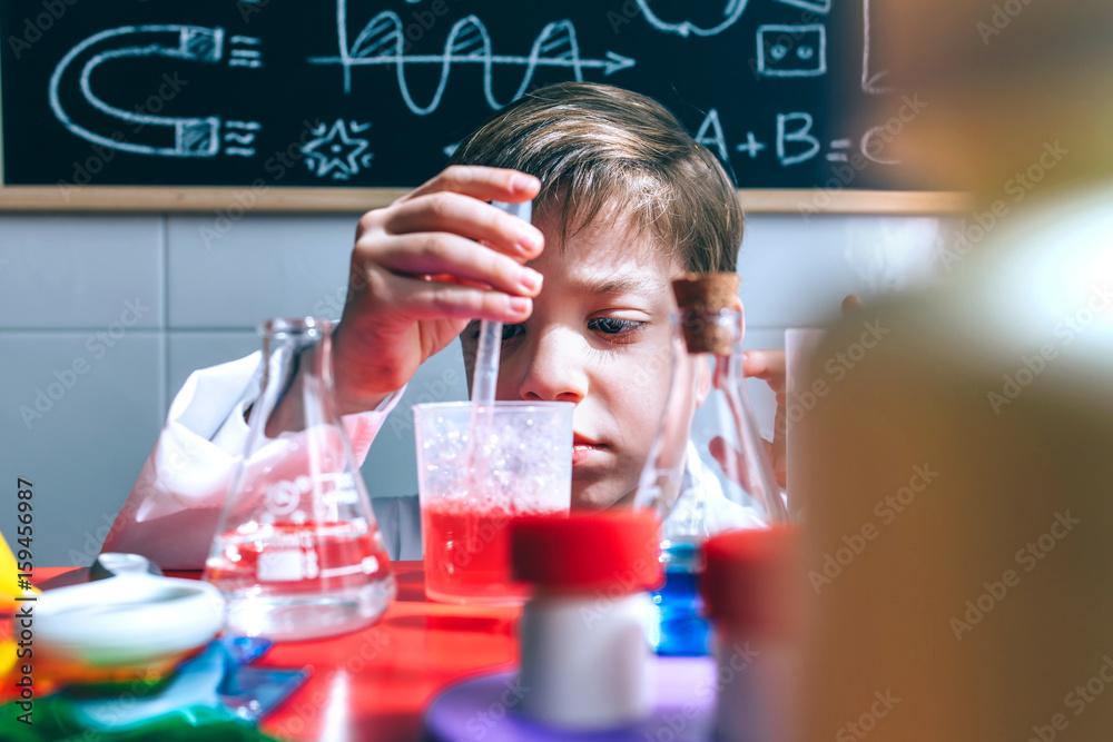 Portrait of little boy scientist extracting red liquid behind of table with chemical toys Portrait of little boy scientist extracting red liquid behind of table with chemical toys