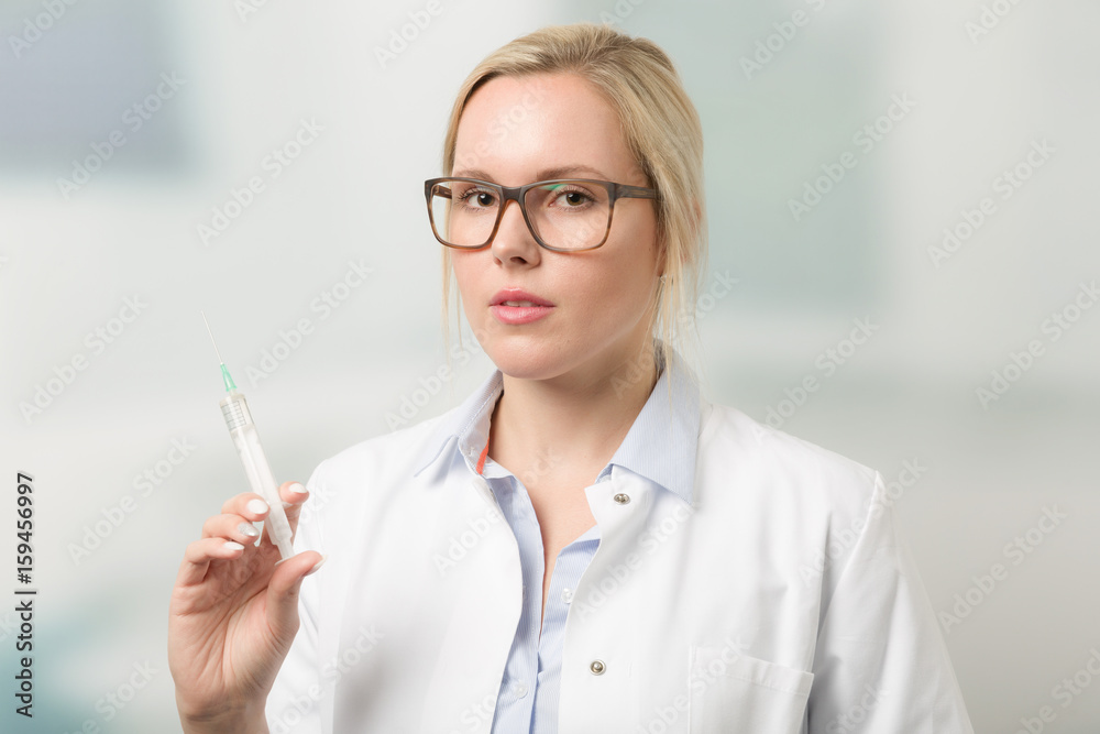 Junge hübsche Ärztin mit aufgezogener Spritze und Praxis im Hintergrund Junge hübsche Ärztin mit aufgezogener Spritze und Praxis im Hintergrund