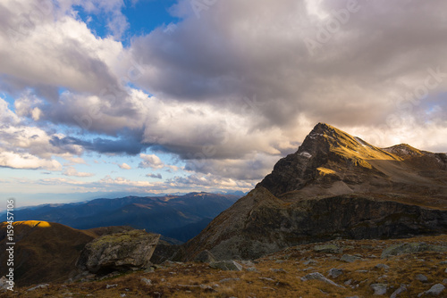 Last warm sunlight on alpine valley with glowing mountain peaks and scenic clouds. Italian French Alps, summer travel destination.