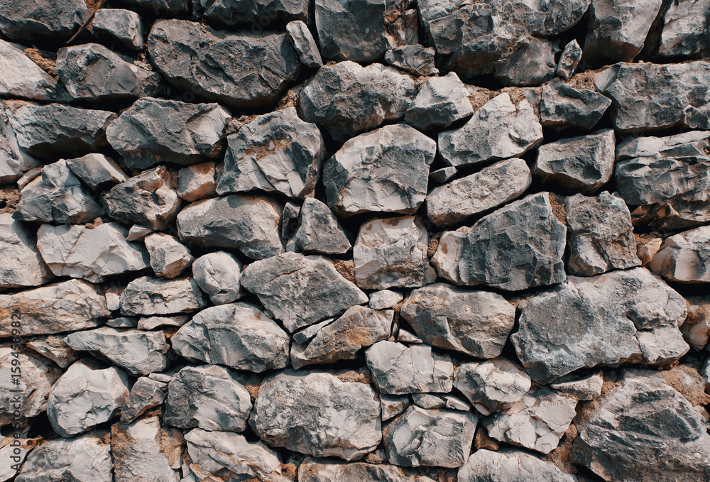 old stone wall consisting of stacked naturally shaped loose rocks - background pattern
