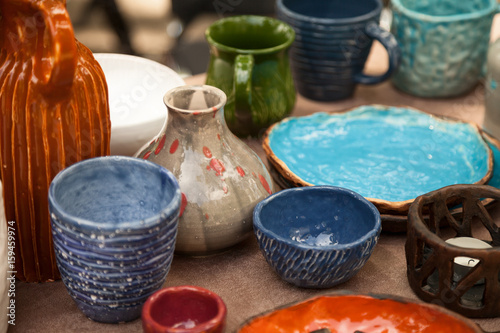 Lots of handmade tableware - ceramic cups, plates at pottery shop. Colorful blue and orange clayware background