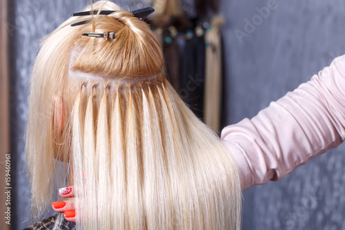 Hair extensions procedure. Hairdresser does hair extensions to young girl, blonde in a beauty salon. Selective focus. photo