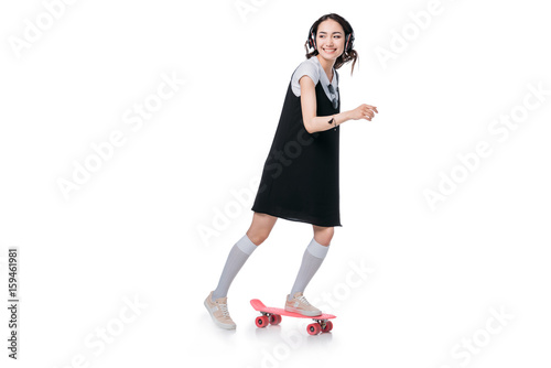 asian girl listening music in headphones and riding on skateboard isolated on white © LIGHTFIELD STUDIOS