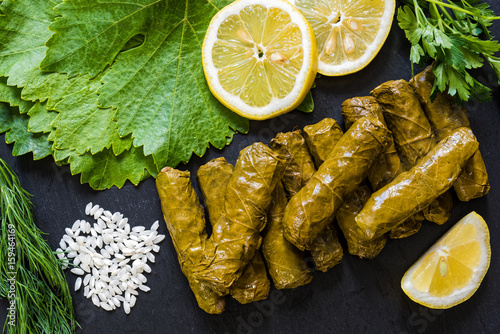 Delicious stuffed grape leaves (the traditional dolma of the mediterranean cuisine) on black dish with leaves, lemon slices, rice, parsley and dill photo