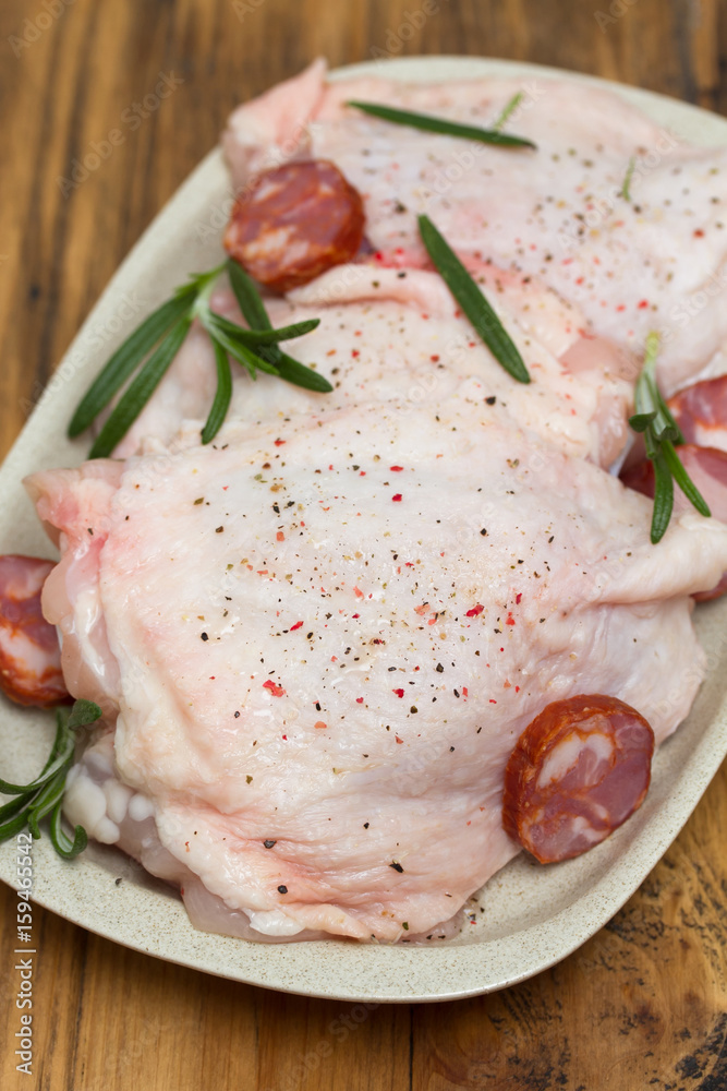 raw chicken with smoked sausage and rosemary on white dish raw chicken with smoked sausage and rosemary on white dish